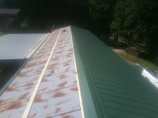 Old rusted panels beside newly installed green metal roofing — Wind Damage Roof Repair by Roofing Brothers in Spring Creek