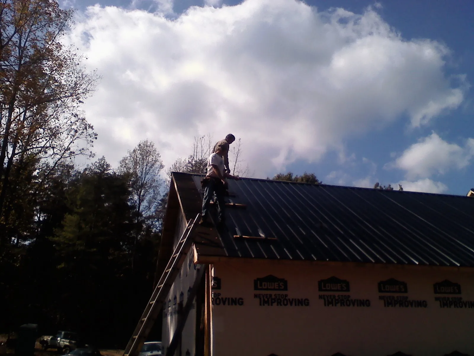Roofer fastening dark metal panels high against a cloudy sky, from a Roof Inspection job in Spring Creek