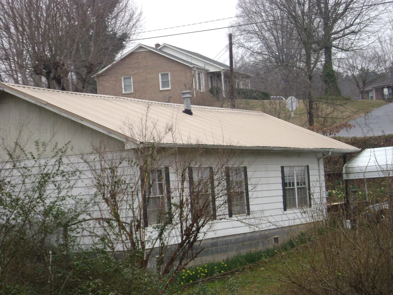 Tan metal roof on a white sided house set into a hillside — Commercial Roofing by Roofing Brothers in Spring Creek
